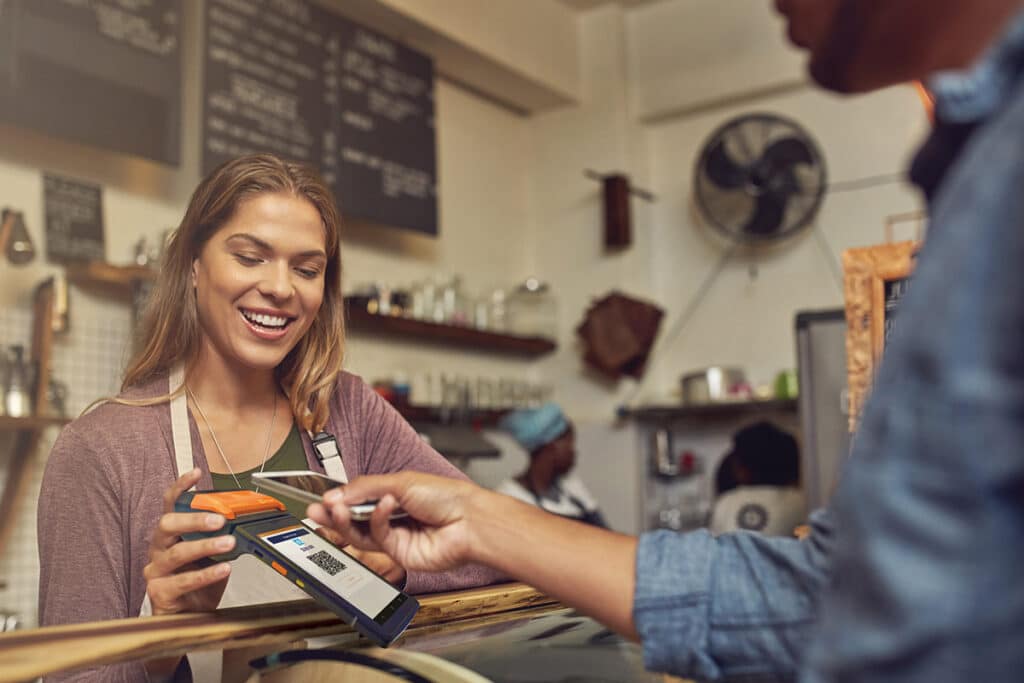 Payment Gateway for small business in Canada: Barista holding an OTT Pay Smart POS Terminal while a customer uses their smartphone to pay