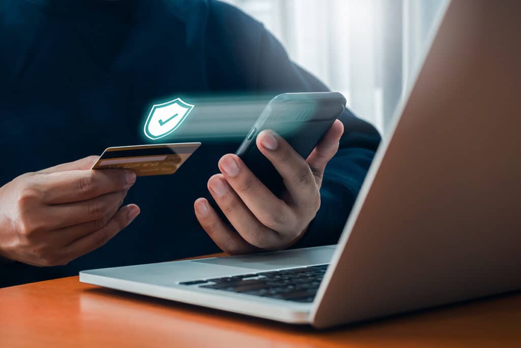 Close up of a person on their laptop, holding a credit card in one hand, and their smart phone in another