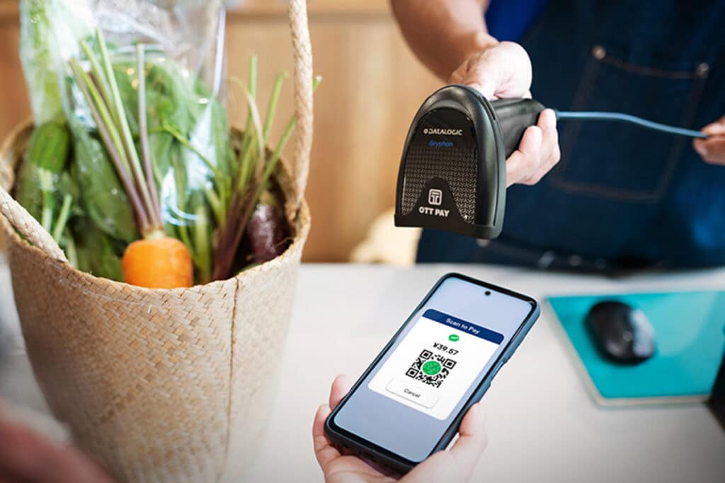 Close up of a merchant using a scanning device to scan a client's QR code on their smartphone
