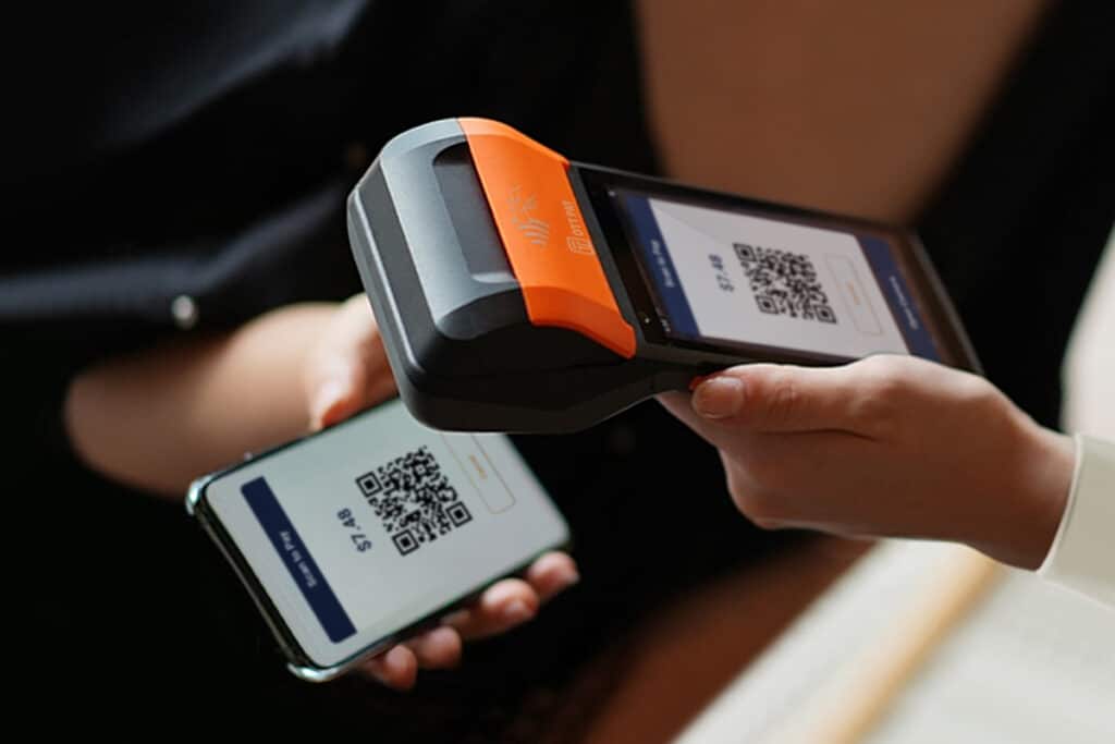 Closeup of someone using an OTT Pay Smart terminal to scan someone's QR code on their smartphone