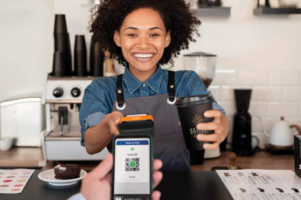 Barista holding up POS terminal in one hand, and offering cup of coffee in another hand
