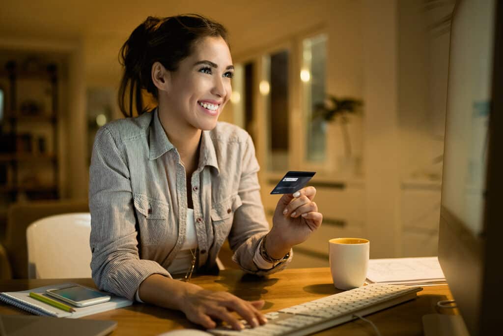 Person on their computer, smiling and holding a credit card