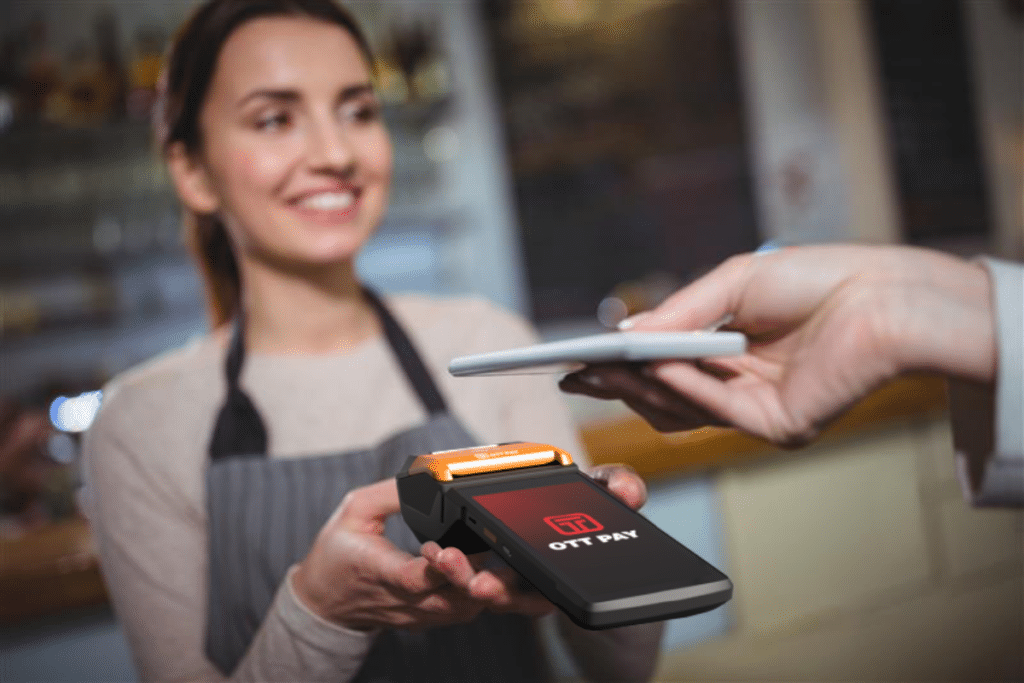 Barista holding up a credit and debit machine while a customer uses their smartphone to pay
